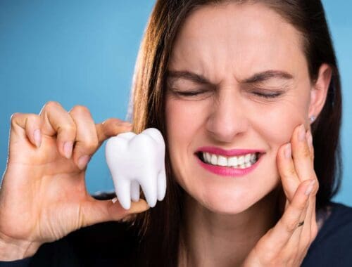 Healthy woman experiencing tooth pain, holding a model tooth, emphasizing dental health and the importance of oral care.