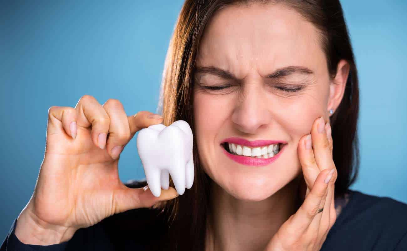 Healthy woman experiencing tooth pain, holding a model tooth, emphasizing dental health and the importance of oral care.
