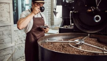 Freshly roasted coffee beans in a commercial roaster at a coffee shop or roastery with a barista tasting coffee, emphasizing healthy living through quality coffee brewing.