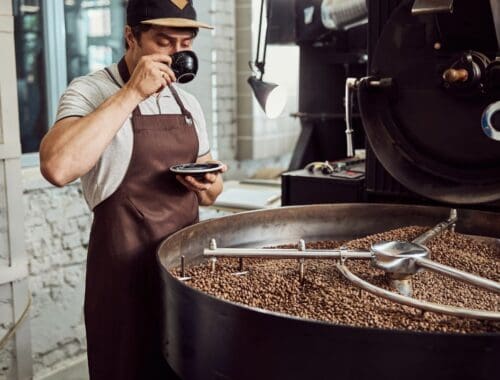 Freshly roasted coffee beans in a commercial roaster at a coffee shop or roastery with a barista tasting coffee, emphasizing healthy living through quality coffee brewing.