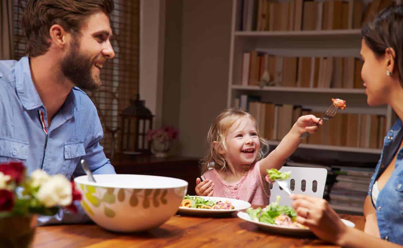 Healthy family meal with smiling parents and child enjoying food together at the dinner table.