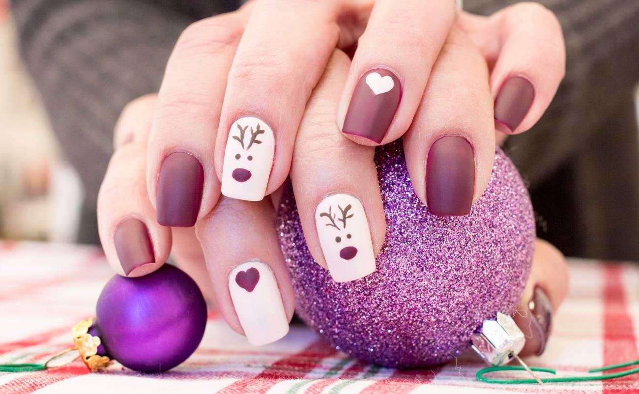 Nail art featuring festive reindeer and heart designs with matte mauve polish, holiday-themed glitter ornaments, and a cozy, colorful background. Perfect for celebrating the holiday season with style.