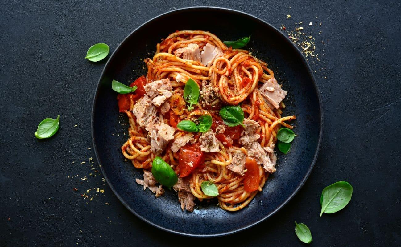 Savory spaghetti with tuna, cherry tomatoes, and fresh basil on a black plate against a dark textured background healthy meal option for balanced diet.