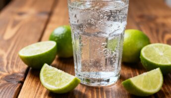 Refreshing glass of sparkling water with lemon-lime wedges on wooden surface, promoting hydration and healthy lifestyle practices.