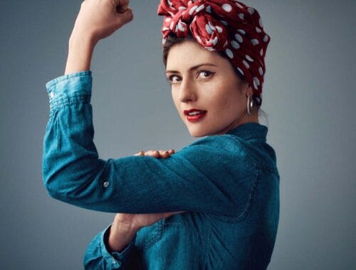 Strong woman flexing her arm, wearing a red polka dot headscarf and denim jacket for health and fitness empowerment.