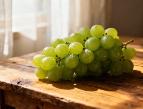 Green grape bunch on a rustic wooden table with sunlight streaming through a window, showcasing fresh, healthy fruit perfect for a nutritious diet.