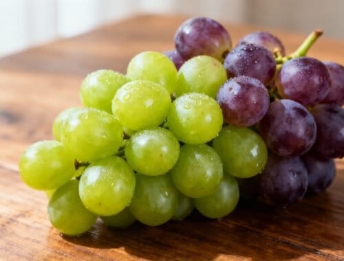 Green and purple grapes on wooden surface, fresh and dew-covered, healthy snack or ingredient for salads and recipes, captured in natural light, vibrant fruit for fitness and wellness diets.