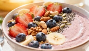 Fresh berry smoothie bowl topped with strawberries, blueberries, banana slices, almonds, chia seeds, hemp seeds, and pumpkin seeds, served in a white bowl for a nutritious breakfast.