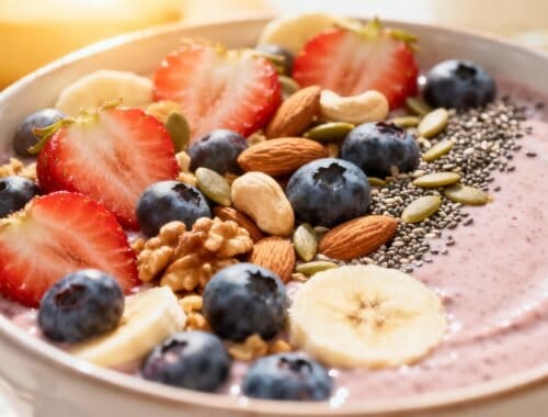Fresh berry smoothie bowl topped with strawberries, blueberries, banana slices, almonds, chia seeds, hemp seeds, and pumpkin seeds, served in a white bowl for a nutritious breakfast.