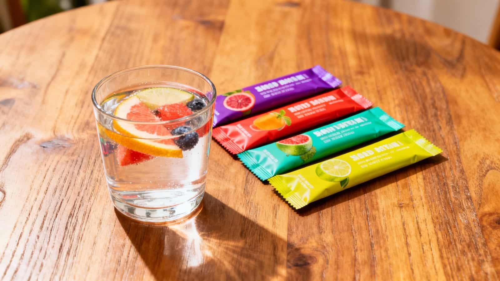Refreshing glass of infused water with lemon, berries, and grapefruit on a wooden table, with colorful healthy snack bars nearby, promoting hydration and nutritious snacking options.