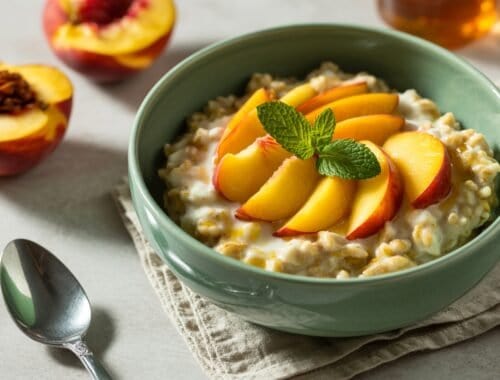 Fresh peach slices over creamy oatmeal with a mint garnish, served in a green bowl for a nutritious breakfast option.