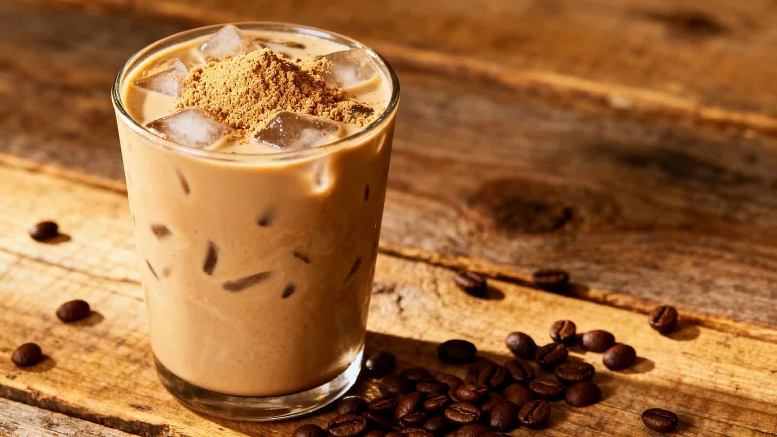 Coffee iced beverage with cream, ice cubes, and a sprinkle of cinnamon on top, served in a clear glass on a rustic wooden surface.