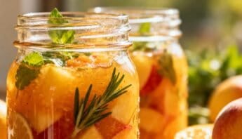 Fresh homemade peach and herb infused water in glass jars, featuring peaches, mint, and rosemary, designed for healthy hydration and wellness.