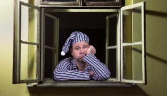 Restless man in pajamas and nightcap sitting at an open window, looking tired and bored, with a disappointed expression, suggesting sleep deprivation or insomnia.