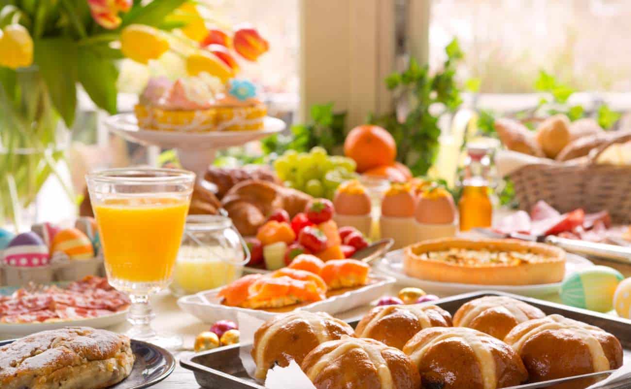 Crispy breakfast pastries and colorful Easter eggs on a table with juice and pastries, bright spring sunlight, cheerful festive breakfast scene.