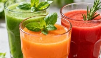 Fresh green, orange, and red vegetable and fruit smoothies with herbs in transparent glasses for healthy nutrition and wellness.