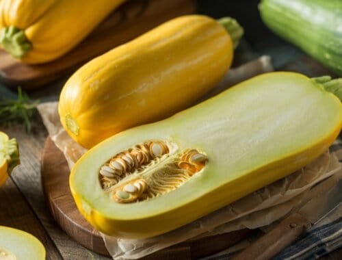 Fresh yellow zucchini cut in half showing seeds, with whole zucchini beside it, on a rustic wooden surface for healthy eating and culinary inspiration.