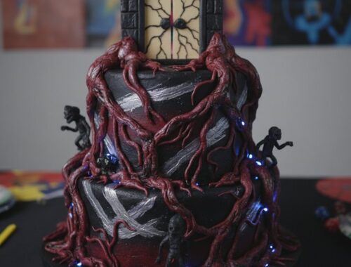An elaborately decorated cake featuring a dark color scheme, twisted red vines, and miniature vampire figurines, perfect for themed parties or Halloween celebrations.