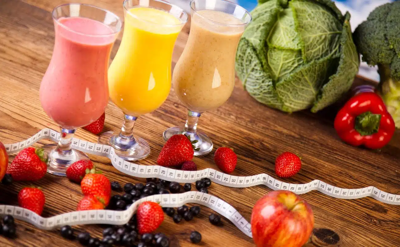 Fresh fruit smoothies with strawberries, blueberries, and apple, surrounded by fresh vegetables like cabbage, broccoli, and red bell pepper, on a wooden table for a healthy diet.