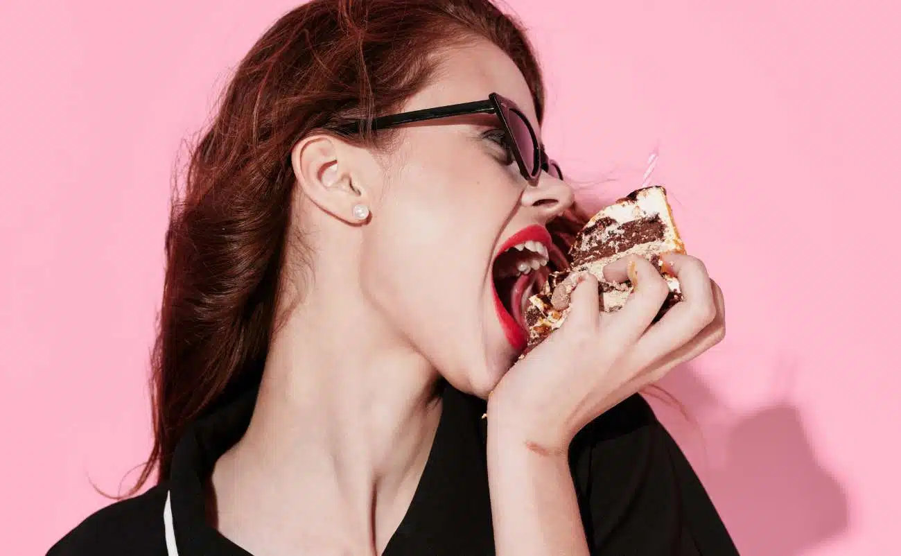 High cholesterol woman eating cake pink background, unhealthy eating habits, sugar cravings, indulgence, dietary temptations, health risks, lifestyle choices, modern diet challenges, nutrition, wellness, diet tips, health and fitness concepts.