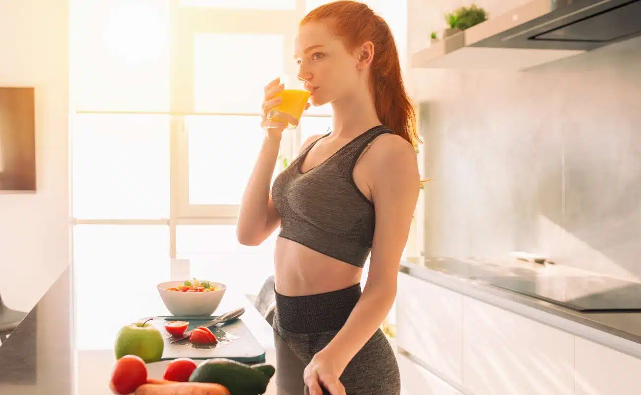 Fresh young woman drinking orange juice in a bright modern kitchen after workout or healthy breakfast, fitness, health, wellness, healthy lifestyle, nutrition, clean eating, active living, morning routine, healthy habits, athletic woman, wellness motivation, morning ritual, healthy eating, fitness lifestyle, nutritious breakfast, lifestyle wellness, healthy mornings, fitness routine, food and drink, vibrant health, healthy choices, morning fitness.