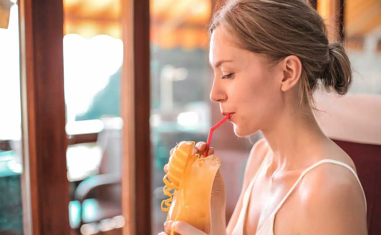 Fresh fruit smoothie in a tall glass with a red straw, young woman enjoying a healthy snack in a cozy café setting.