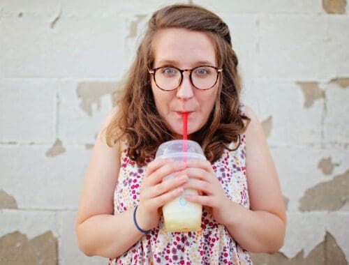 Refreshing homemade lemonade being enjoyed by a young woman with glasses and curly hair on a textured brick wall background.