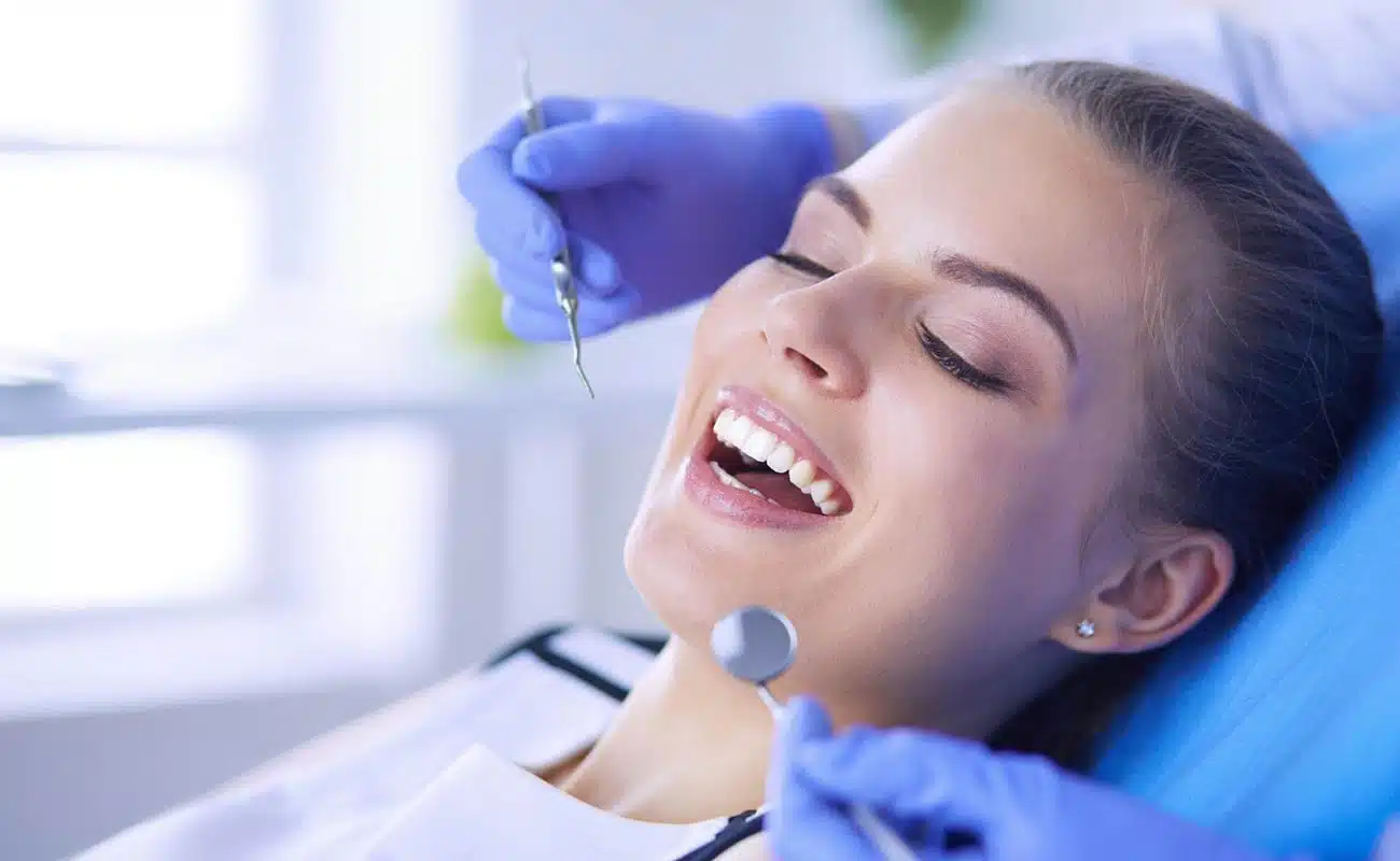Teeth whitening procedure at dentist's office, close-up of smiling woman during dental treatment with bright smile and dental tools, emphasizing dental health and cosmetic dentistry services.
