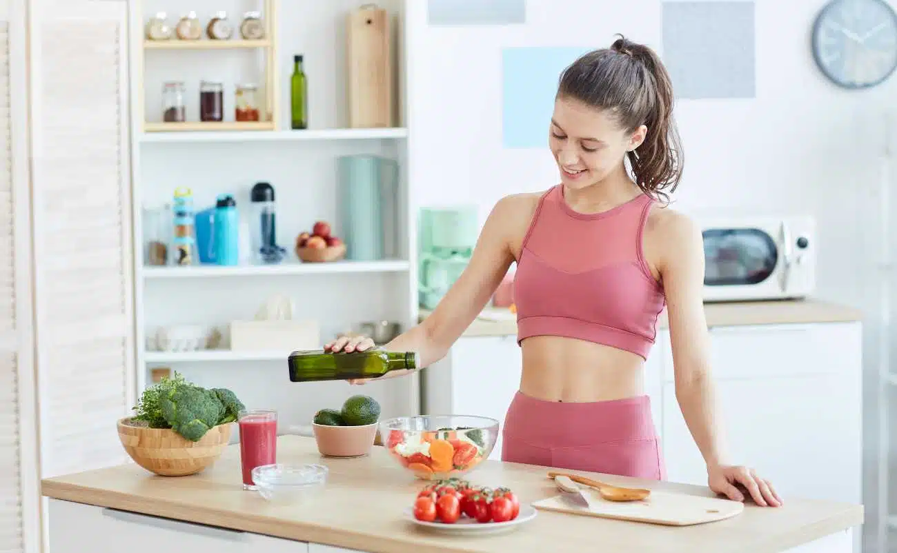 Fresh vegetable salad preparation by woman in pink activewear in bright modern kitchen.